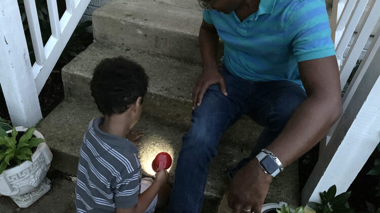 一个小男孩用手电筒照着台阶，他的父亲在夜间探索时在一旁看着。