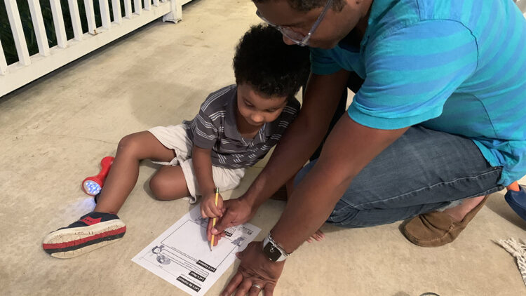 一对父子在夜间探索时分享他们的观察结果，并在观察图上一起写下他们的想法。