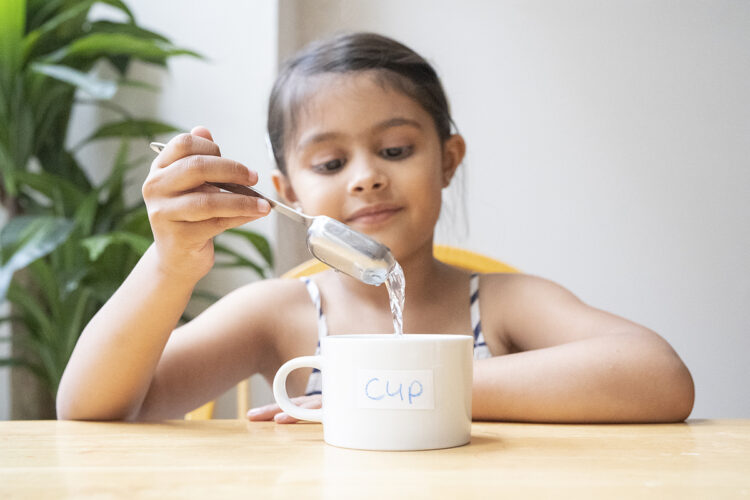 孩子用汤匙装满一个杯子的容器。