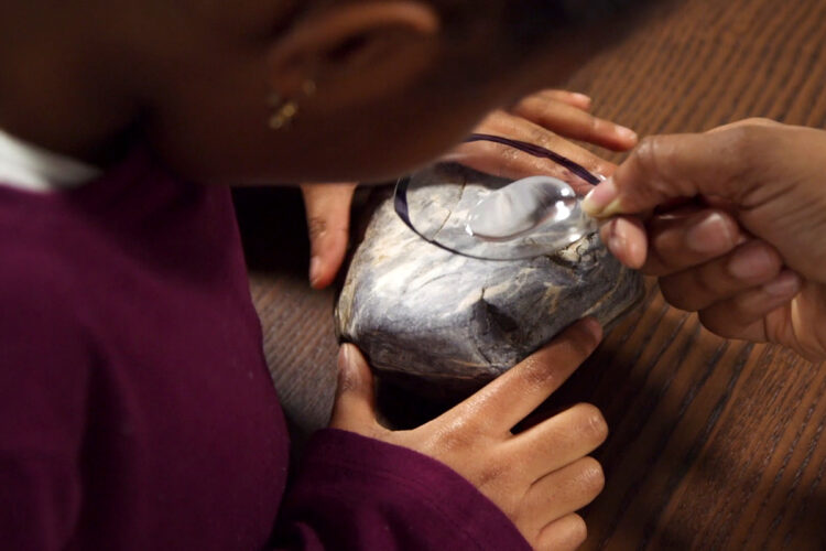 女儿将儿童放大镜举到岩石上进行放大镜观察。